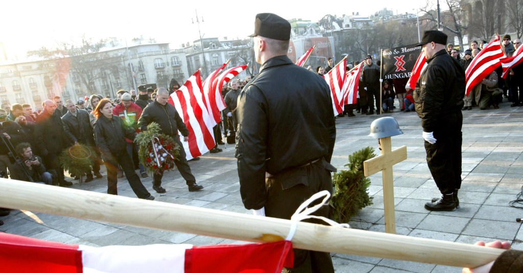 Hungarian activists of the neo-Nazi Blood and Honour group hold flags in Budapest 11 February 2006 as participants bring wreaths at the tomb of Unknown Soldier in Heroes Square in Budapest where a German WWII helmet and wood cross were placed. More than 600 people attended the event to commemorate the 60th anniversary of the ill-fated escape attempt of Nazi German and Hungarian soldiers from Buda Castle, which was besieged 11 February 1945 by the Soviet Red Army at the end of World War II. (Photo by ATTILA KISBENEDEK/AFP via Getty Images)