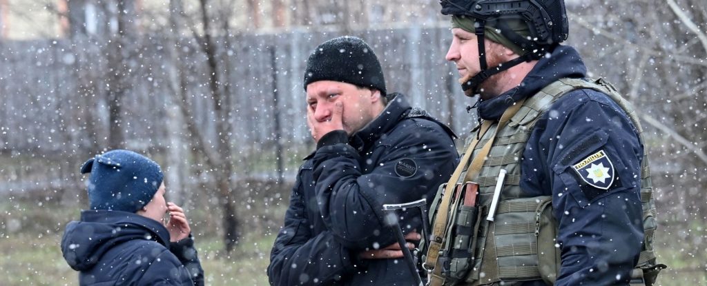 People react as they gather close to a mass grave in the town of Bucha, just northwest of the Ukrainian capital Kyiv on April 3, 2022.