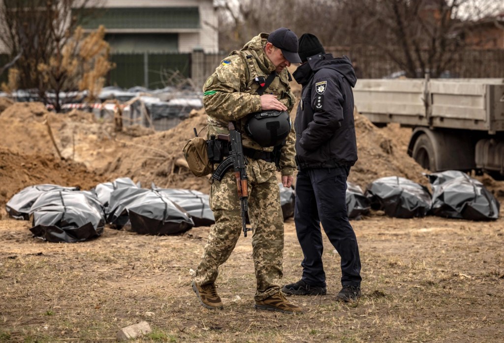 A member of the Ukrainian army and a policeman stand near body bags exhumed from a mass grave where civilians where buried in Bucha, on the outskirts of Kyiv, on April 13, 2022, amid Russia's military invasion launched on Ukraine. - A visit by the International Criminal Court's chief prosecutor to Bucha -- the Kyiv suburb now synonymous with scores of atrocities against civilians discovered in areas abandoned by Russian forces -- came as the new front of the war shifts eastward, with new allegations of crimes inflicted on locals. (Photo by FADEL SENNA/AFP via Getty Images)