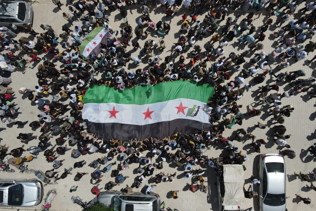 Overhead shot of large Syrian flag surrounded by people.