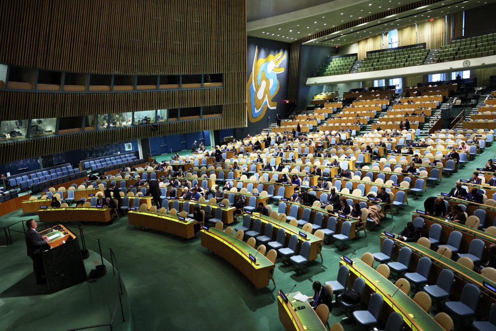 Wide-angle shot of an assembly hall at the United Nations with nations' representatives in tiered seats.