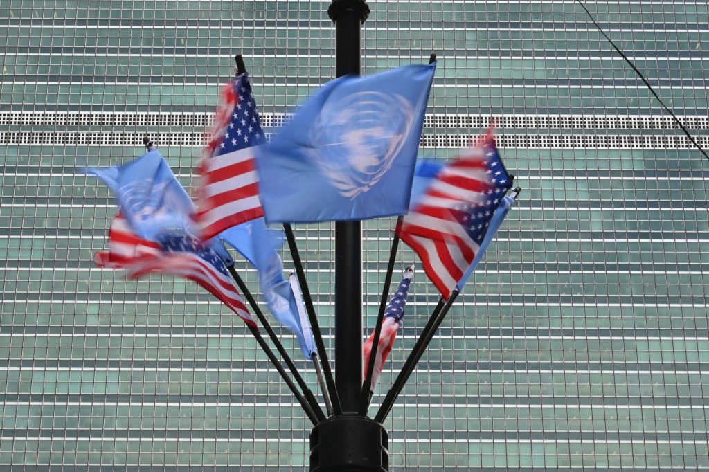 Alternating American flags and United Nations flags, set around a pole, wave in the wind.