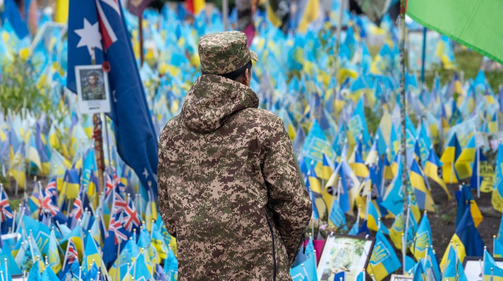 A man stands in front of a wall of blue and yellow Ukrainian flags.