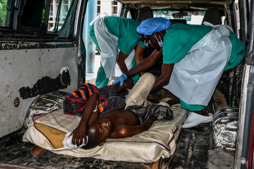An injured boy lays on his back in a van as two others attend to his wounds.