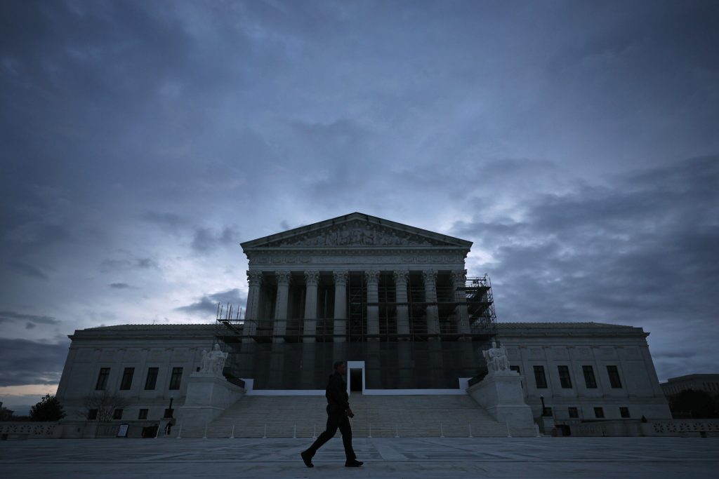 A man walks in front of the Supreme Court building at dusk.