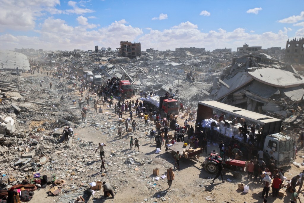 Palestinians rally around aid trucks which entered from the Karem Abu Salem crossing, in Khan Yunis in the southern Gaza Strip on October 12, 2025, as a ceasefire between Israel and Palestinian factions holds in the besieged territory. A Gaza ceasefire was holding for a third day on October 12, ahead of a US-proposed hostage-prisoner exchange and a summit aimed at charting a path to peace after two years of war. (Photo by OMAR AL-QATTAA/AFP via Getty Images)