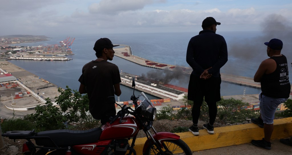 People watch the smoke rising from Port of La Guaira after explosions and low-flying aircraft were heard on January 03, 2026 in La Guaira, Venezuela. According to some reports, explosions were heard in Caracas and other cities near airports and military bases around 2 am. US President Donald Trump later announce that his country's military had launched a "large-scale" attack on Venezuela and captured its President Nicolas Maduro and his wife. (Photo by Jesus Vargas/Getty Images)