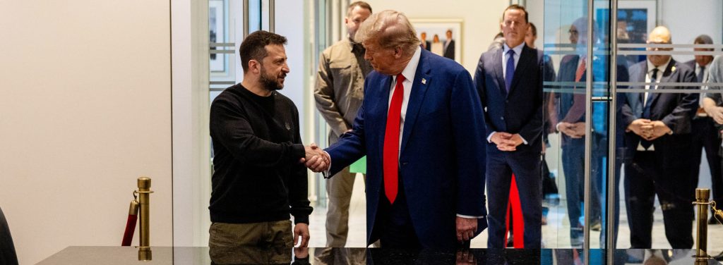 The photo shows the two men standing inside a door behind a long table, their reflection showing on the shiny tabletop, with their aides in the background.